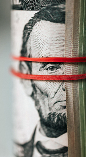 A rolled up five dollar bill showing half of Abraham Lincoln's face with a rubber band above and below his eye